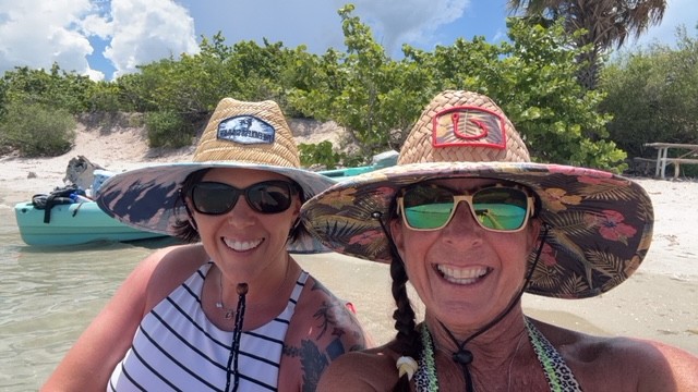 Lisa and Terina smiling in sunglasses on a sunny beach day